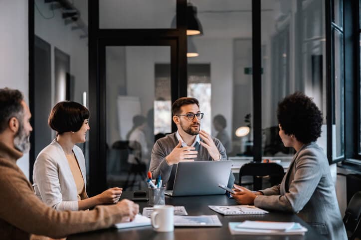 A business leader is explaining a project to his team while sitting in a boardroom in a corporate firm.