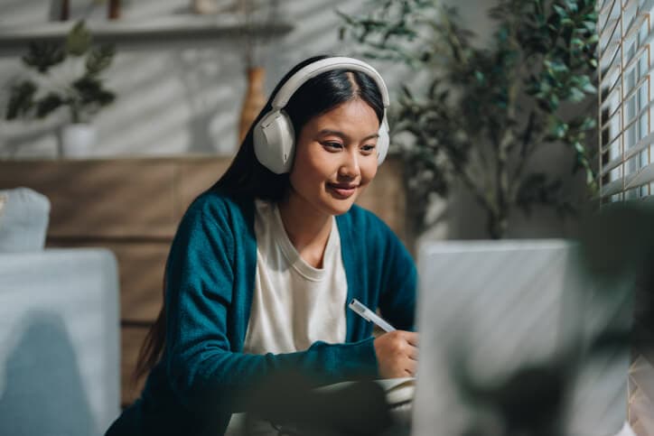 Woman enjoying her online class, attentively taking notes as she stays engaged and focused. With a sense of curiosity and dedication, she embraces the opportunity to learn from home and improve her knowledge.