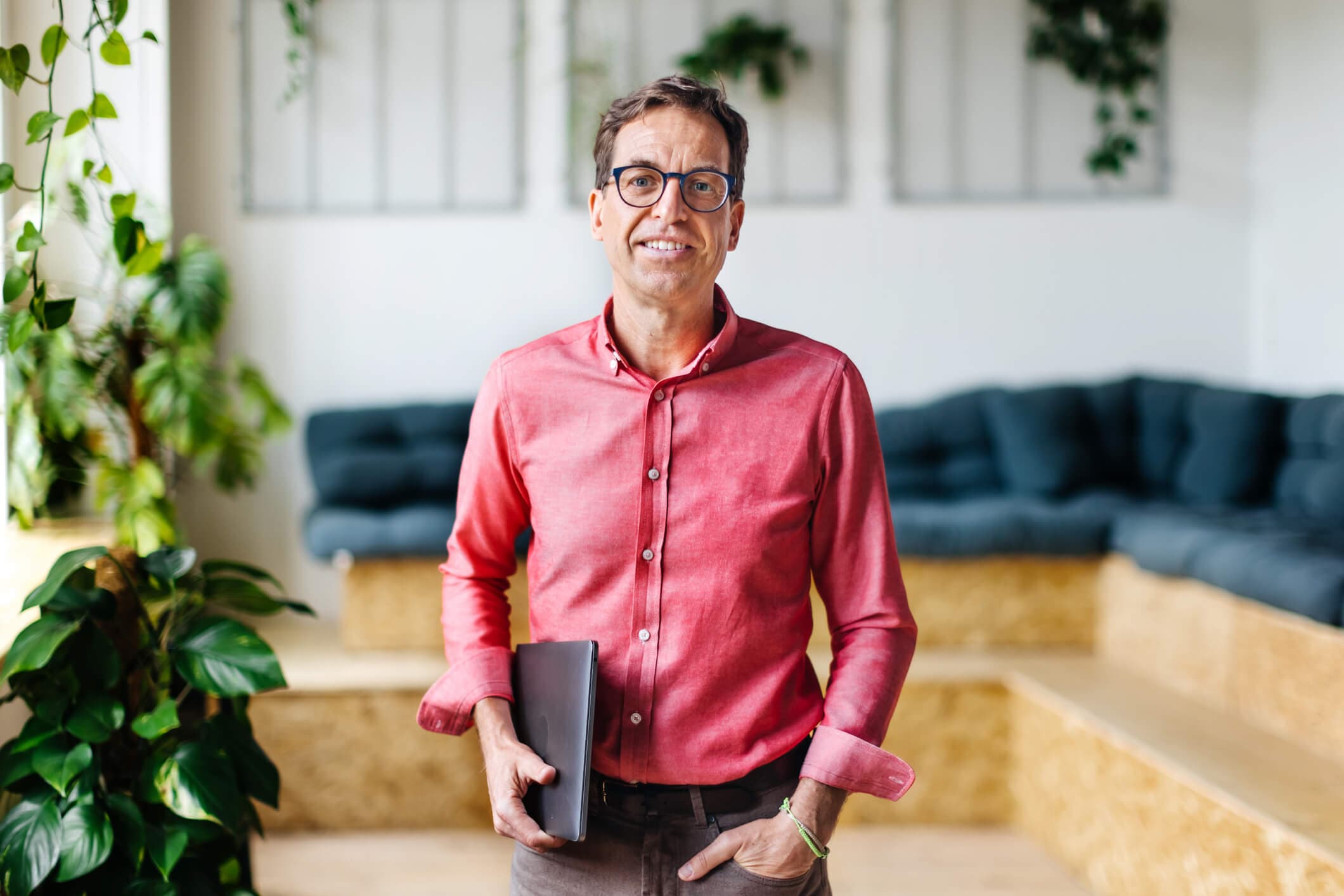 A smiling business leader wearing a red shirt and holding his laptop under his arm.