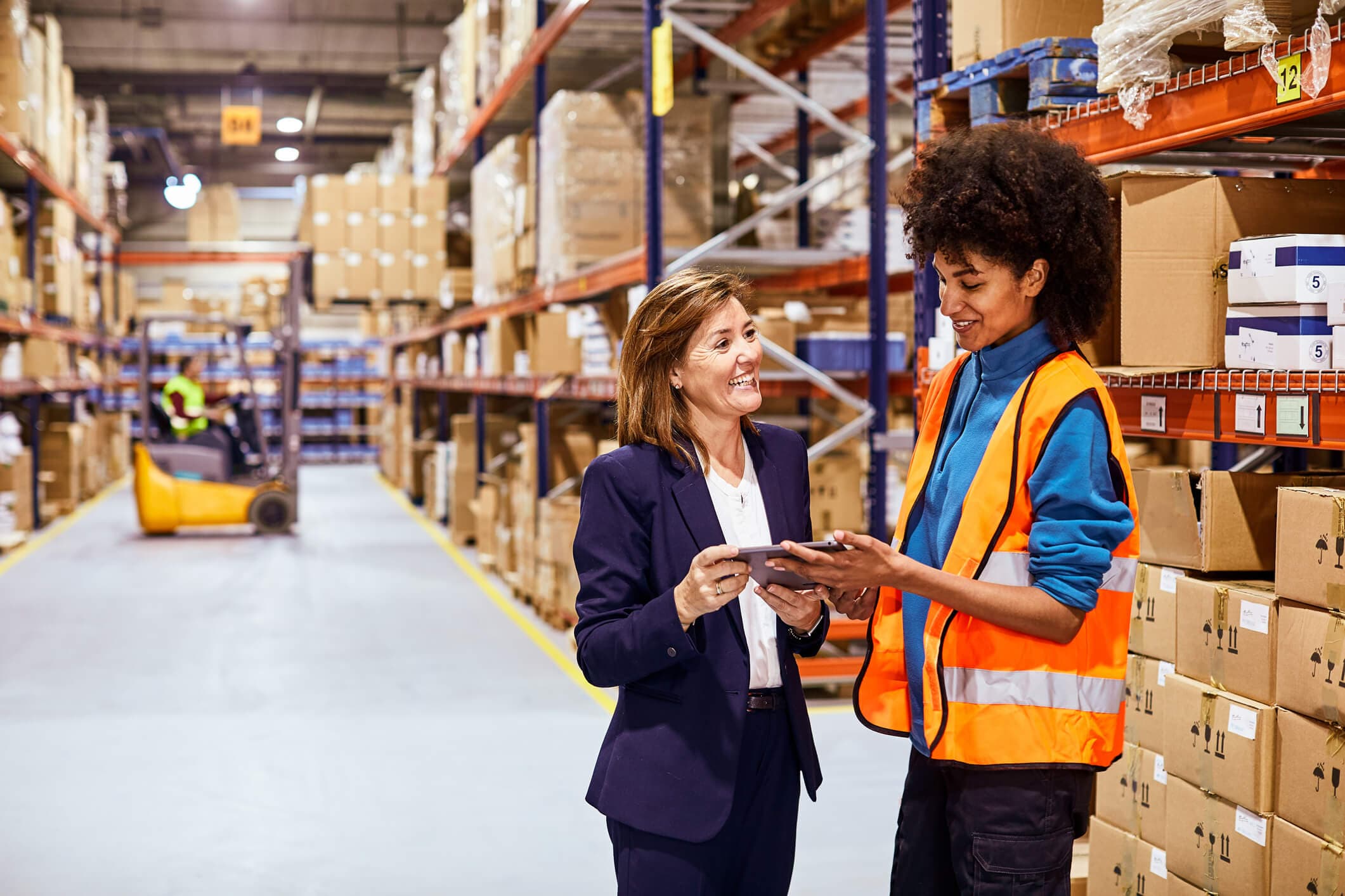 A female senior supply chain manager has a discussion with a female team leader in a distribution warehouse.