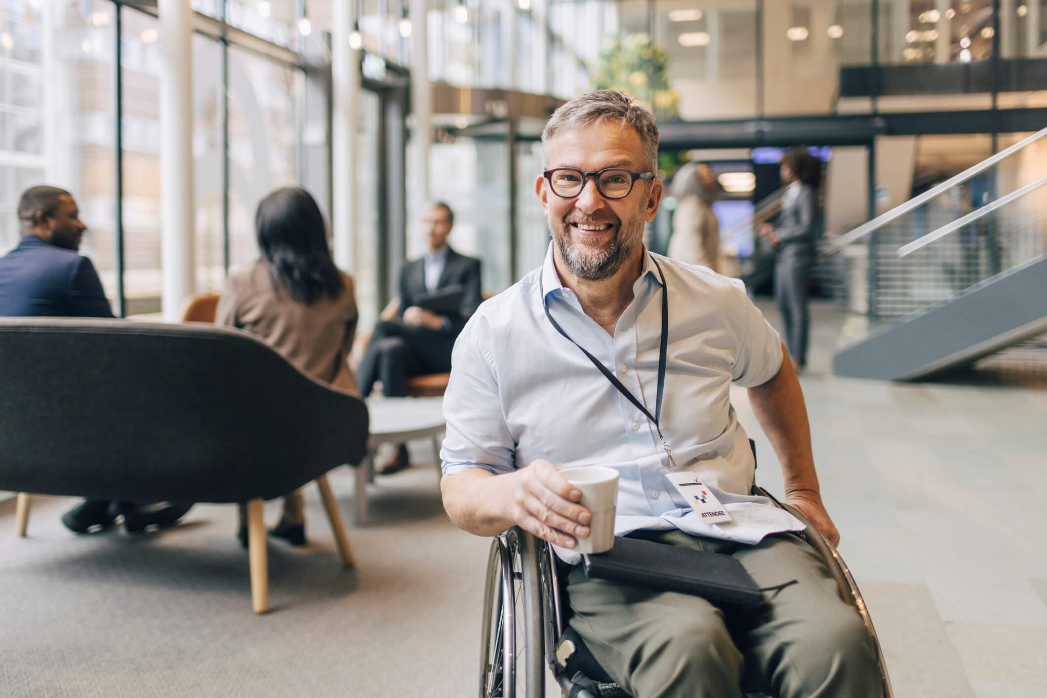 Businessman in a wheelchair holding a coffee cup while taking a break from networking at a business convention.