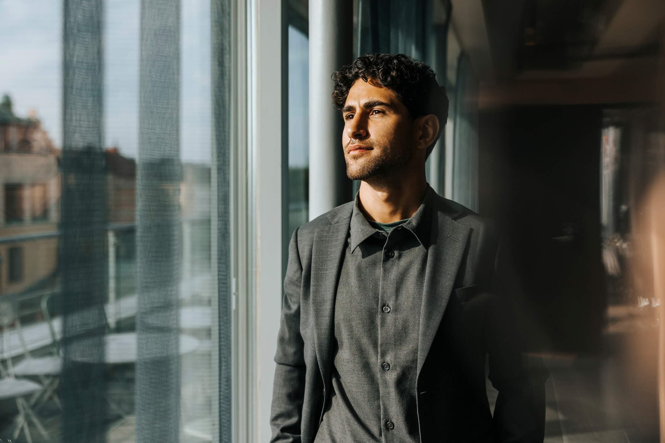 Thoughtful young male entrepreneur looking through glass window at office.