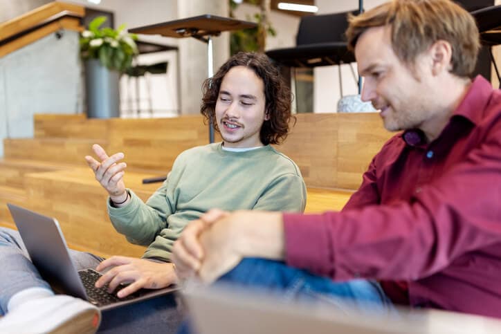 Young man talking with colleague looking at laptop in creative office.