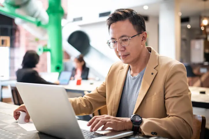Mid-aged Asian Chinese male professional in a business suit working on his laptop computer in the office.