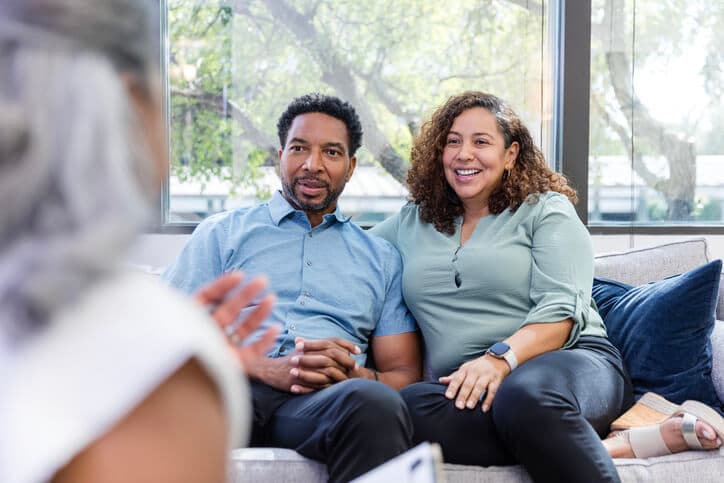 Mature adult couple listening to advice from a senior female marriage therapist in the foreground of the photo.