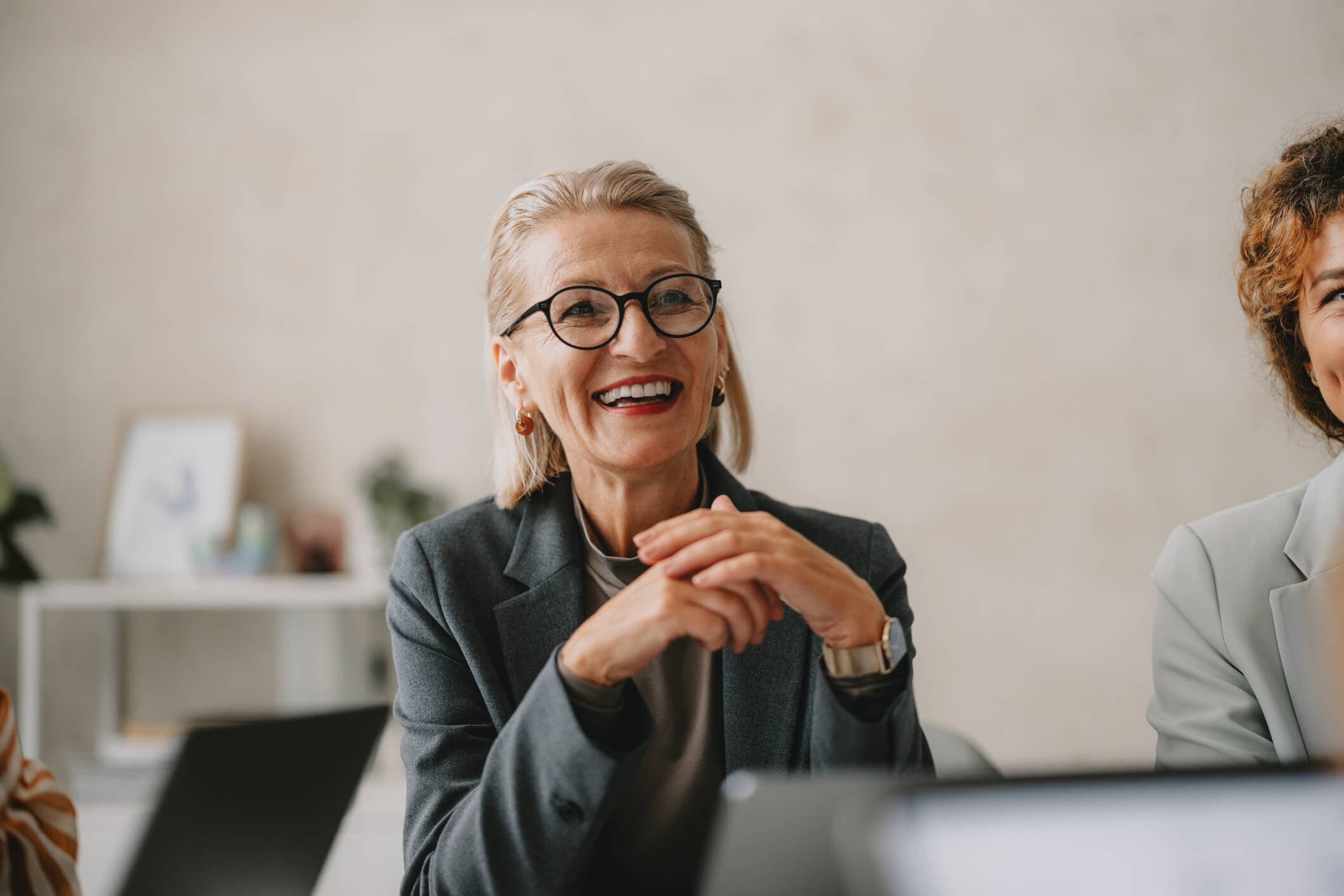 Smiling senior business leader in glasses conversing with a colleague during an office meeting.