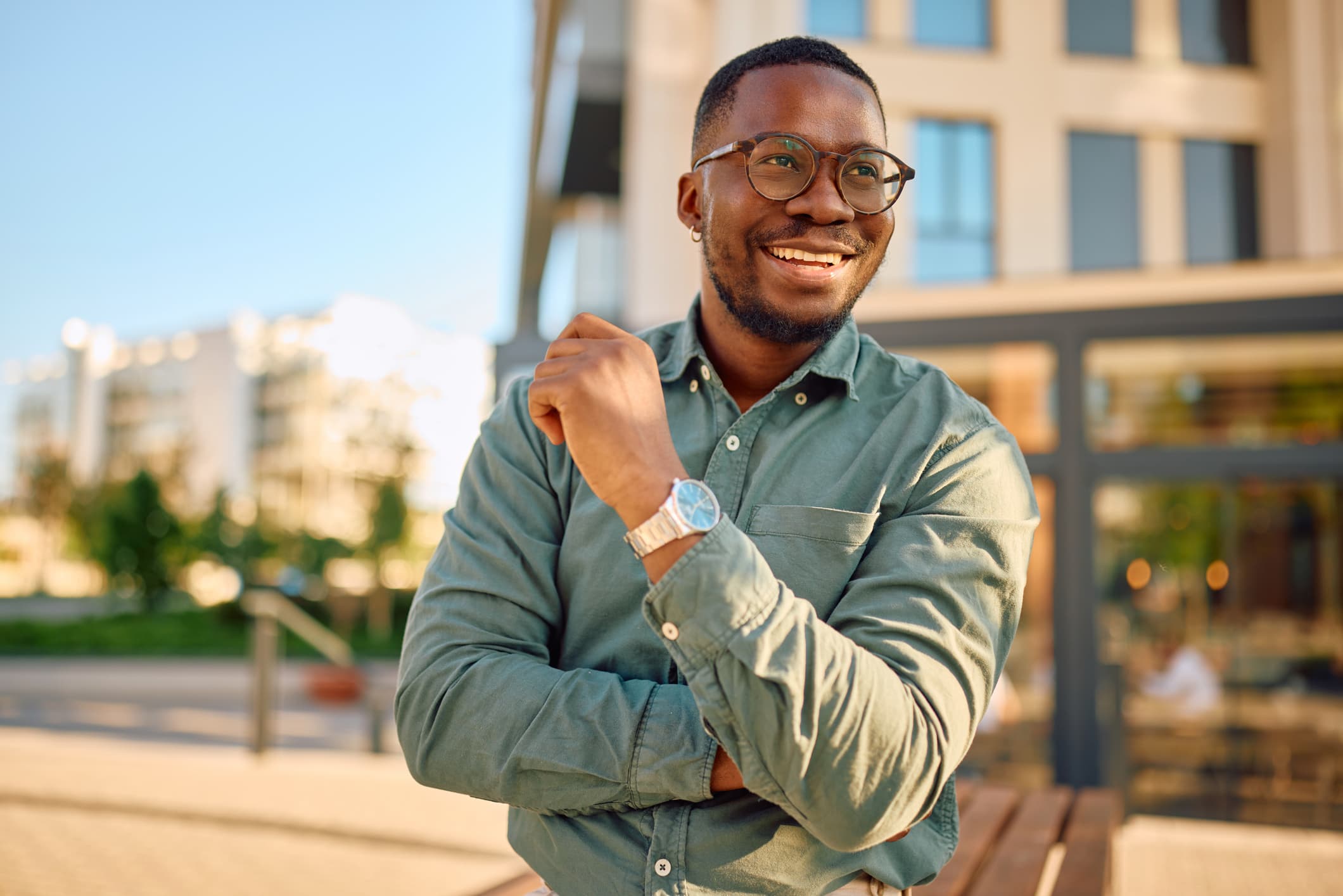 Portrait of a confident and successful young African American businessman smiling and looking away while standing with his arms crossed in a modern city setting.