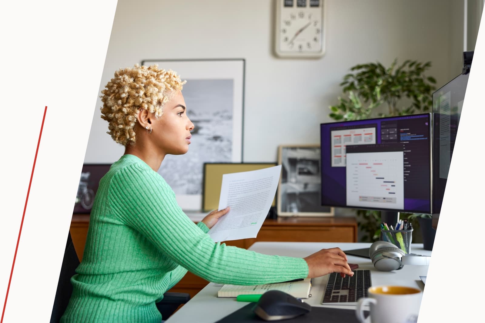 Woman holding paperwork and looking on her desktop.