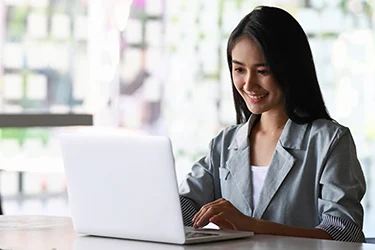 Woman smiling as she is typing and looking down at laptop